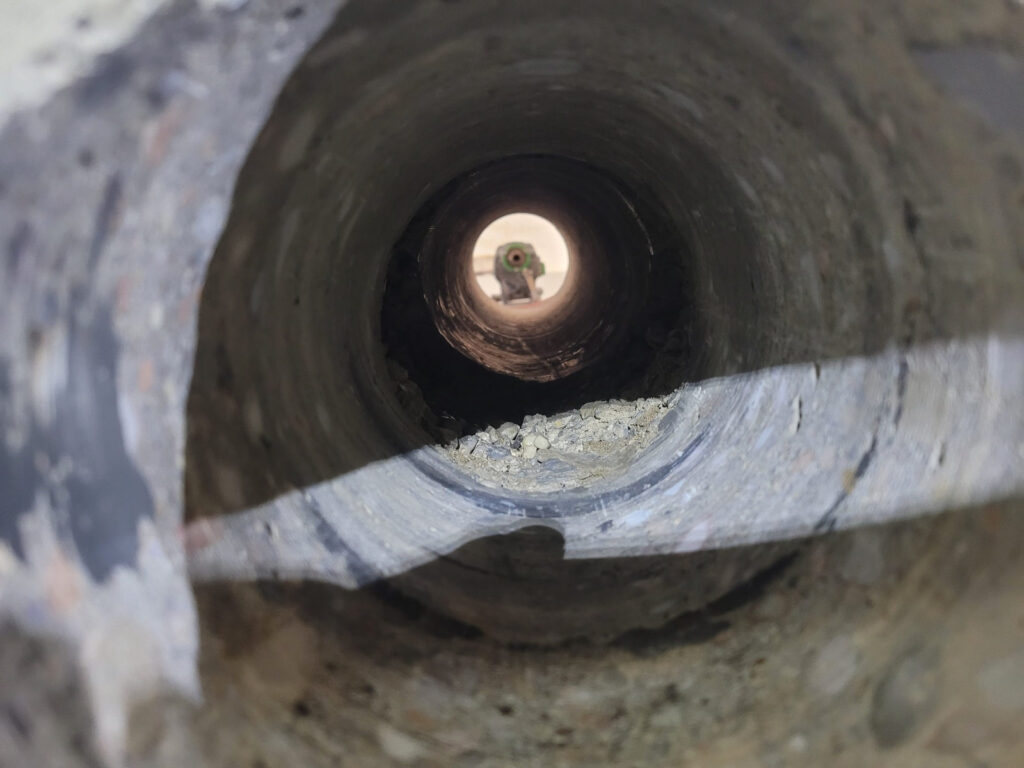 Deep concrete core-drilled opening connecting a basement and crawlspace through separate foundation walls for radon mitigation